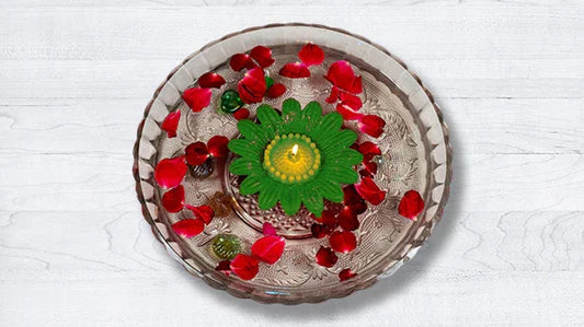 Green flower-shaped floating candle with red rose petals in a glass bowl on white background