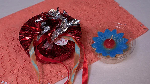 Blue flower-shaped candle with red center and round red gift box on pink lace cloth