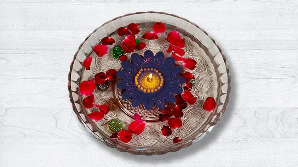 Floating blue flower candle with red rose petals in a glass bowl on a white surface