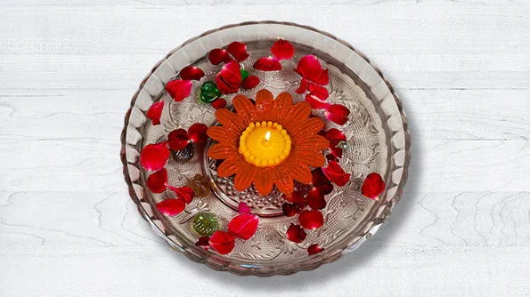 Orange flower-shaped candle floating in glass bowl with rose petals on white background